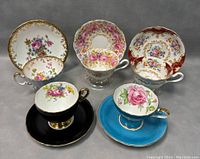 Photo showing all five porcelain bone china tea and saucer sets arranged in a semicircle with a gray background, highlighting floral patterns and gold trim.
