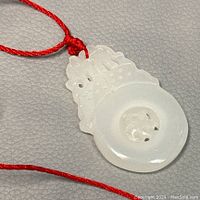 Close-up image of the white jade carved pendant showing the circular central section and intricate top design, suspended on a red cord.