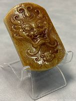 Close-up photo of the rectangular jade belt buckle showing detailed dragon carving with rich brown and yellow hues.