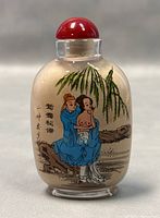 Front side of the clear glass snuff bottle showing two figures seated under a tree with Chinese calligraphy