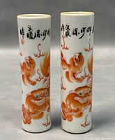 Front view of the pair of cylindrical Chinese porcelain vases showing hand painted orange mythical creatures and black calligraphy.