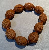 Full view of the stretchy bracelet composed of carved olive seed beads shaped into Buddha faces with smaller plain beads in between.
