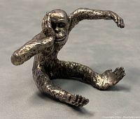 Close-up photo of the silver sitting monkey sculpture, showing textured fur and facial detail with one arm reaching forward.