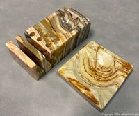 View of vintage carved onyx or marble desk accessory set including a multi-functional ashtray and pen holder and a separate small tray, showing natural banded stone pattern in earthy tones.