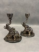 Two vintage sterling silver elephant shaped weighted candleholders with trunks raised holding candle cups, placed on gray background.