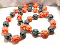 Photo showing the flexible massage rope workout hula hoop composed of orange and gray ribbed massage balls connected in a chain forming a loose loop on a white surface.