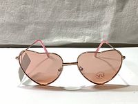 Front view of heart shaped sunglasses showing rose colored lenses and rose gold metal frame with nose pads.