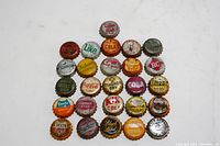 Photo of 26 vintage bottle caps laid out in rows on a flat surface showing the diverse branding and colors of the collection.