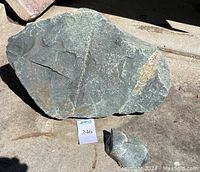 Two large green and grey rocks with a small rock visible on concrete floor with auction lot number card.