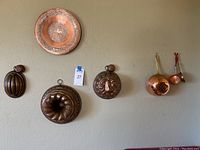 Wide view showing five antique copper molds of different designs hanging on wall, Turkish-style copper plate, and two small copper skillets