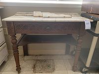 Full front view of the carved wood washstand with white marble top and drawer, showing carved floral detailing and turned legs.