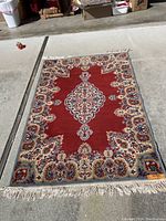 Top-down view of rectangular red and cream area rug laid flat showing central medallion and floral border patterns with fringed edges.