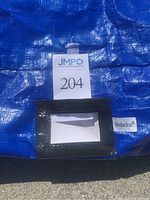 Close-up of Belador brand tag attached to blue woven plastic with black zipper and product ID tag.