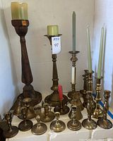 Large assortment of brass and wood candlesticks with some candles and snuffers included.