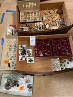 Overview photo of multiple jewelry pieces arranged in trays and boxes, showing earrings, bracelets, necklaces, and pendants in assorted styles and colors.