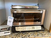Cuisinart Exact Heat CTO-390 toaster oven with metal insert tray on top placed on kitchen counter. Stainless steel body with digital control panel and glass door visible.