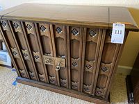 Front view of Drexel wooden bar cabinet with carved panels and decorative metal hardware, key latch visible in the center.