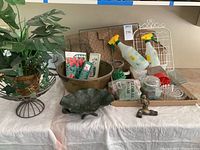 Overview of all garden and floral items on display including the brass pot, wire basket, lily pad bowl with frog, glass coasters, floral foam, sprayers, and seed packets.