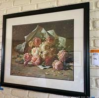 Full view of framed print showing bouquet of pink and white flowers wrapped in paper, hung on white brick wall.
