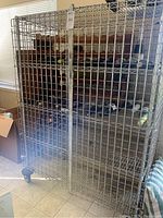 Front view of large metal wire storage cage with double doors closed, placed indoors near window.