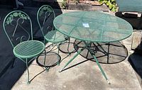 Overall view of round green metal patio table with two matching chairs on concrete surface showing wear and rust spots.