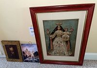Framed religious art print with Virgin Mary and child Jesus in red wooden frame, Carmel mission tile, and Rembrandt print on wood shown together on carpet.