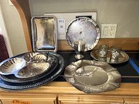 Overview photo showing multiple silver plated serving pieces including divided dish, trays, and drinking vessels.