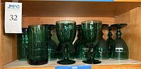 Shelf display showing 12 dark green stemmed goblets and 3 highball glasses on the right side.