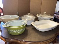 Front view of vintage casserole and baking dish set showing multiple Corning Ware and Pyrex dishes on a table with lids and without.