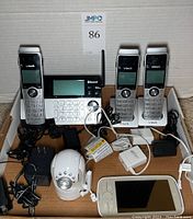 Wide view of the lot showing VTech cordless phone base with Bluetooth and four handsets, Infant Optics baby monitor camera and handheld display, and power cords.