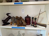 Shelf showing entire group of wood art pieces including carved ducks, model sailboat with canvas sail, candlesticks, round box, petrified wood and small cups.