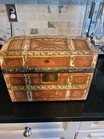 Front view of antique mini chest highlighting painted wood panels, metal trim, and keyhole on lid.