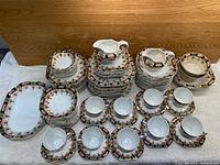 Full view of the Imperial Derby china set, showing all stacked plates, bowls, cups with saucers, and serving pieces arranged by type.