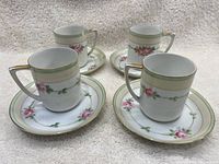 Four Nippon porcelain teacups each paired with matching saucers, showing floral hand-painted rose designs, gold rim accents, and green bands.