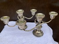 Pair of Kabo Sterling silver three-arm candelabras displayed on a white cloth against a dark background, showing full front and side views highlighting the detailed edges and curves.