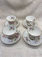 Four Royal Doulton teacups and saucers arranged on a fabric surface, showing floral pattern and overall set composition.