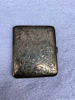 Top side of cigarette case showing intricate engraving of floral and scroll design on sterling silver surface.