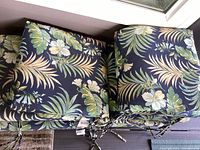 Four stacked tropical outdoor cushions showing folded ties and floral leaf pattern.