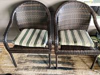 Four black and brown woven patio chairs, two with striped seat cushions, arranged outdoors on patio.