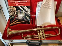 Brass trumpet, music book, sheet music inside a red-lined metal case