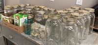 Wide view of many clear Ball Mason jars, including large, medium and small sizes, some with lids.