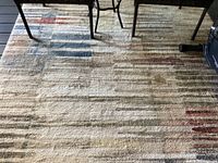 Photo of earth tone indoor/outdoor rug on covered patio showing linear pattern in multiple colors under chairs and exercise bike.