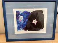 Blue framed Georgia O'Keeffe floral print titled "Black Hollyhock, Blue Larkspur" showing blue and black flowers with a star-shaped center.