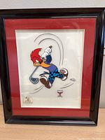 Full view of framed piece showing red mat and black wood frame under glass