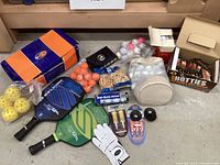 Full lot overview showing golf balls, pickleball paddles and balls, hand warmers, golf tees and glove, and shoe box.