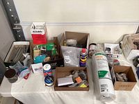 Overview photo showing large roll of plastic sheeting, multiple hardware boxes, WD-40 cans, sanding belts, and various small parts on a table.