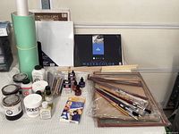 Photo showing various jars of painting mediums including acrylic medium matte and gesso, bottles of drawing inks, multiple packaged paint brushes, art paper pads including watercolour paper by Canson, flat wooden stretcher bars, and bottles of mediums and oils.