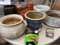 Various planter pots arranged on a table including ceramic, terracotta, and stone-like pots with hummingbird nectar mix and nectar guard tips