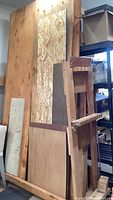 Vertical stack of various wood sheets including plywood and OSB with natural wood grain and chipboard texture behind a wooden chair frame.