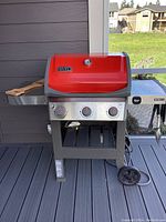 Front view of red Weber Spirit grill on deck, showing lid, three control knobs, cart and wheels